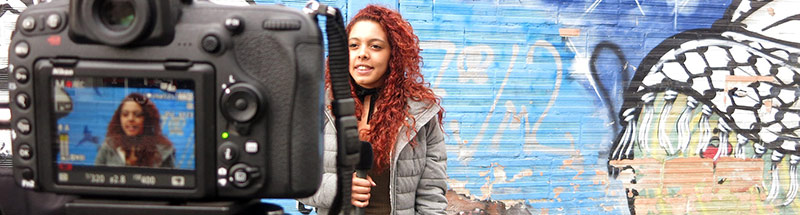 Ein junge Journalistin mit Mikrofon wird vor einer Graffitiwand gefilmt